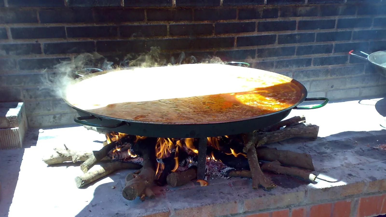 Paellera de arroz cocinándose sobre fuego de leña con las brasas encendidas debajo